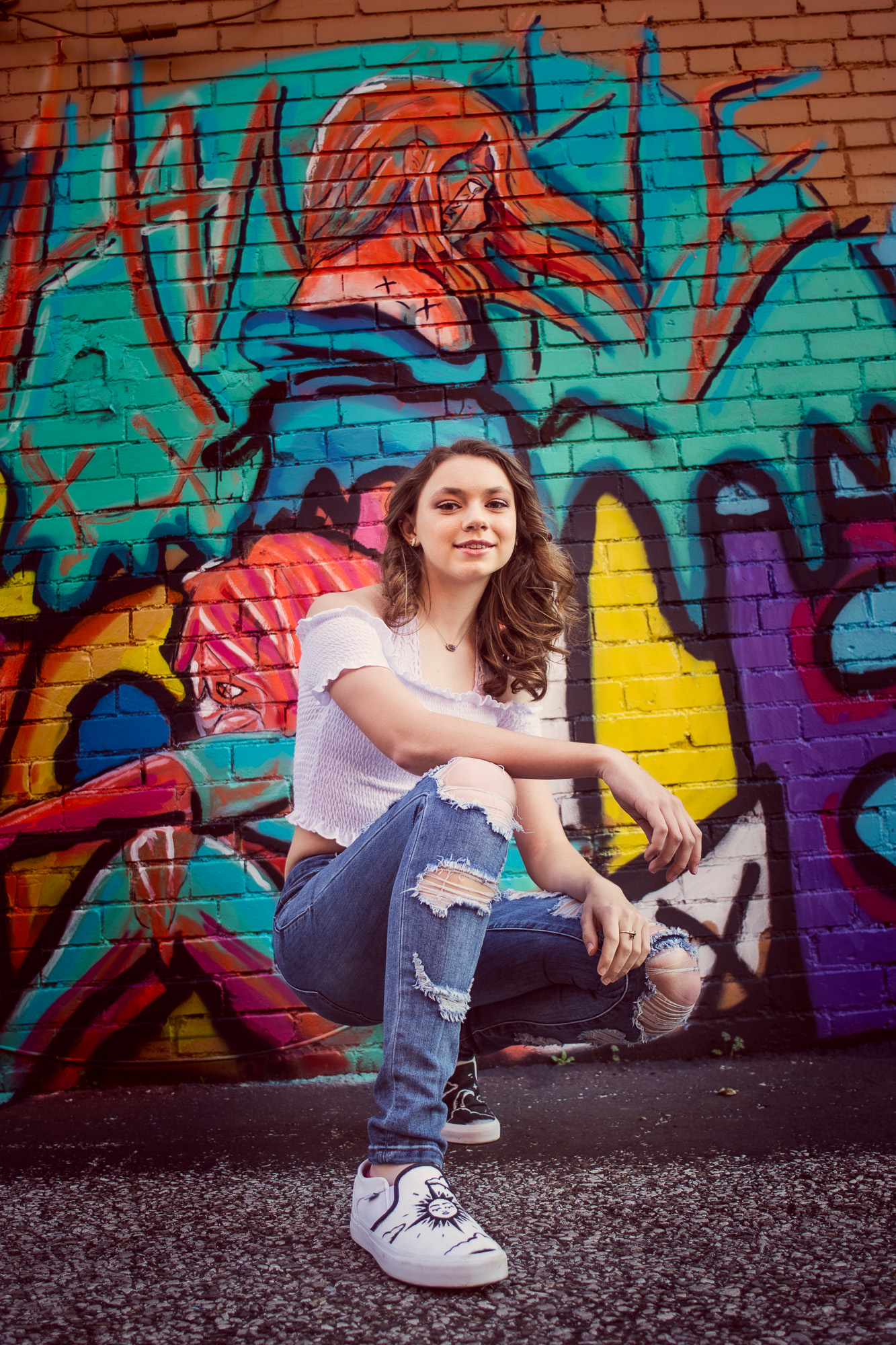 Senior Photos of a girl squatting in front of a graffiti wall in evansville indiana